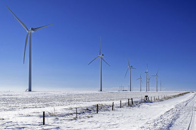Windmills on field against clear sky during winter