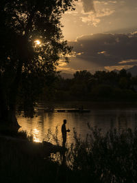 Silhouette people standing by lake against sky during sunset