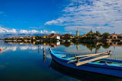Boats moored in lake against blue sky