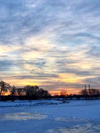 Snow covered landscape against sky during sunset
