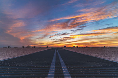 Low angle shot of beach walkway leading sea against colorful sky during sunset