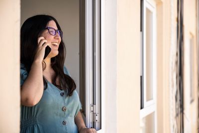 Brunette spanish girl dressed on a business serius look talking on the phone at the window from her apartment during the afternoon in palma de mallorca, spain during coronavirus confinement