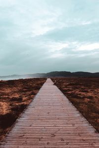 Boardwalk leading towards landscape against sky