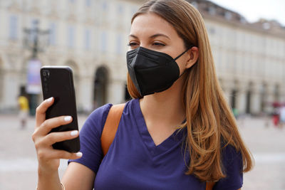 Close up of girl with black protective mask ffp2 kn95 using smart phone with urban background