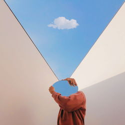 Person holding mirror against sky