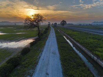 Road amidst field against sky during sunset