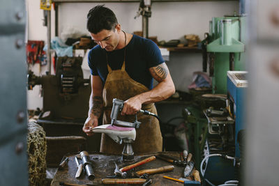 Confident shoemaker making shoe on workbench while standing in workshop