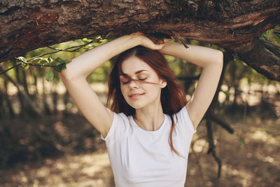 Beautiful young woman standing by tree trunk