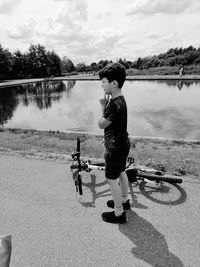 Full length of boy standing by bicycle against lake