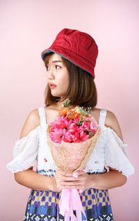 Young woman holding pink flower against white background
