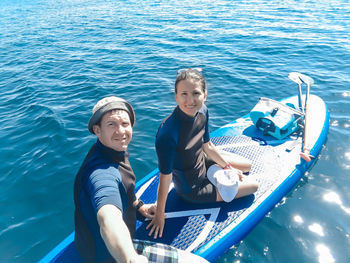 High angle portrait of friends sitting on paddleboard in sea