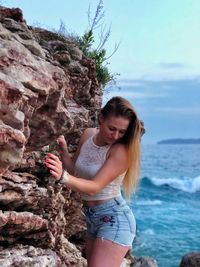 Young woman looking away while rock in sea against sky