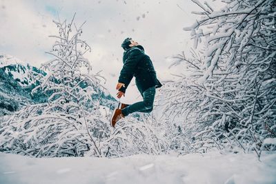 Side view of young man jumping on snow covered field in forest