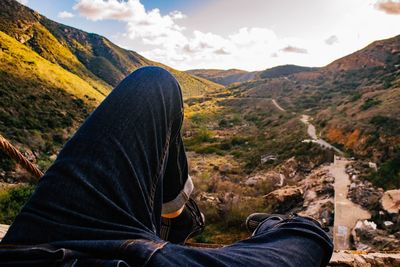 Man sitting on mountain against sky