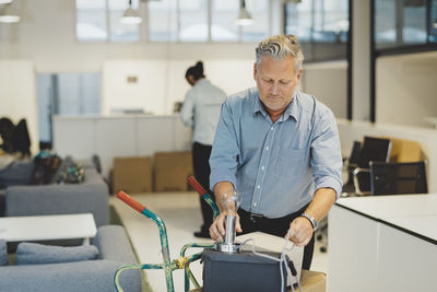 Mature businessman arranging desk lamp on box in new office