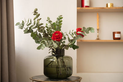 Silver eucalyptus with red roses in a dark glass vase stands on the table in the room
