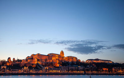 Illuminated buildings by river against sky