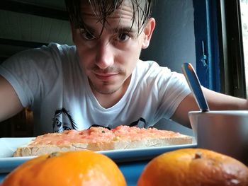 Portrait of young man having food while sitting by window at home