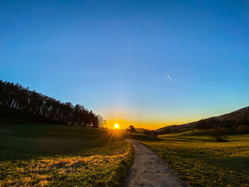 Road amidst field against sky during sunset