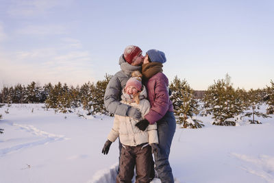 Kissing parents embracing cute daughter in snow during winter