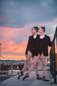 Woman standing by railing against sky during sunset