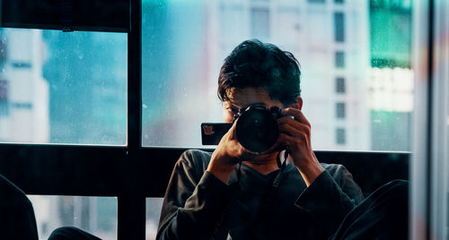 Portrait of woman photographing through window