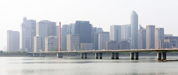 Modern buildings by river against clear sky in city