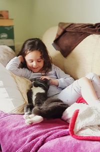 Full length of girl playing with cat on bed at home