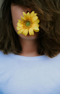 Anonymous woman with hair covering face holding daisy flower in her mouth