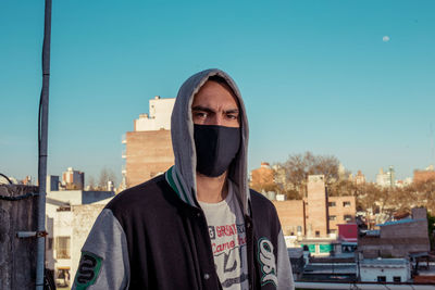 Portrait of young man with face mask in city against clear sky