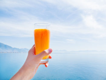 Hand with fresh tasty freshly-squeezed juice of ripe oranges in glass. seascape. kemer, turkey.