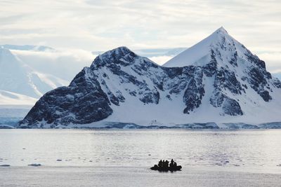 People on snowcapped mountain by sea against sky