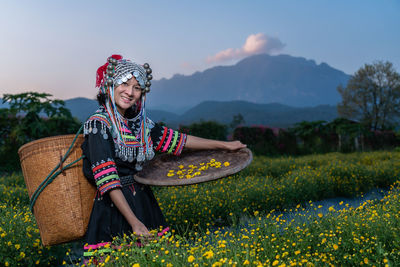 Portrait of smiling woman in traditional clothing holding wicker basket while standing in farm