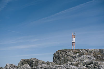 Girl standing on rock formation against blue sky on sunny day