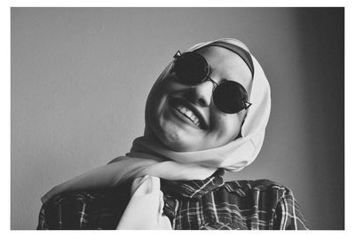 Smiling young woman wearing sunglasses and scarf against wall 