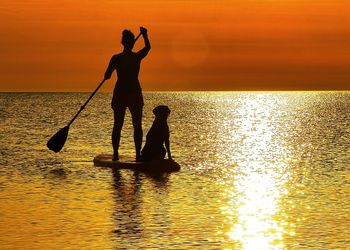 Silhouette men in sea against sky during sunset