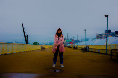 Rear view of woman wearing hood standing on footpath against sky at dusk