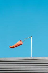 Low angle view of weather vane on roof against clear blue sky