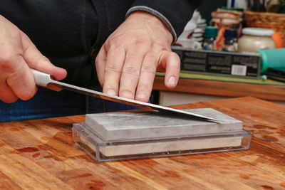 Cropped hand of person sharpening knife on table