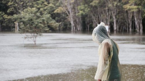 Side view of woman wearing raincoat while standing by lake during rainy season