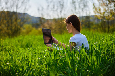 Rear view of woman using mobile phone while sitting on grassy field