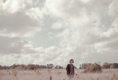 Woman standing on field against cloudy sky