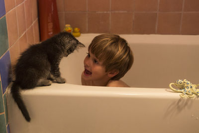 Boy with cat sitting in bathtub at home