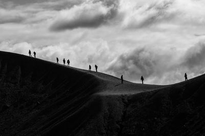 People walking on road against cloudy sky