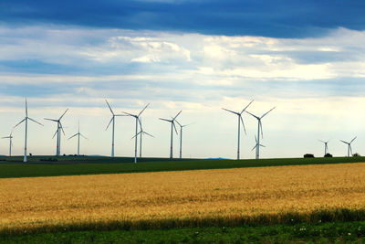 Wind turbines on field against sky