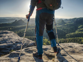 Happy man hiker hold medicine stick, injured knee fixed in knee brace feature. scenic mountain top 