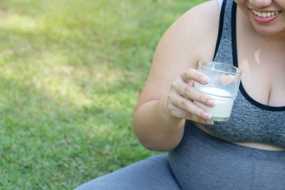 Midsection of pregnant woman smiling while having drink at park
