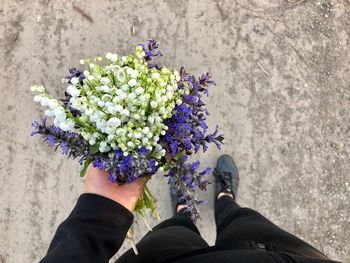 Low section of woman holding flowers while standing on road