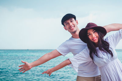 Portrait of smiling romantic couple with arms outstretched standing at beach