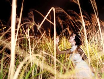 Side view of woman wearing white dress standing amidst grass at night